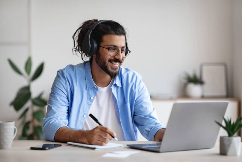 Man sitting in front of his laptop with headphones on smiling
